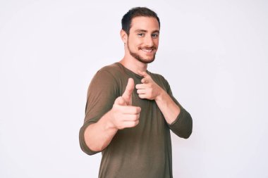 Gündelik giysiler giymiş genç yakışıklı adam mutlu ve komik yüzüyle kamerayı işaret ediyor. iyi enerji ve titreşimler. 