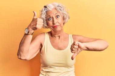 Kıdemli, gri saçlı, günlük kıyafetler giyen, baş parmak kaldıran, anlaşmazlık ve anlaşma ifadesi olan bir kadın. çılgın çatışma 