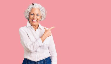 Son sınıf gri saçlı, günlük kıyafetler giyen, neşeli yüzlü, elleri ve parmaklarıyla gülümseyen mutlu ve doğal bir ifade takınan bir kadın. 