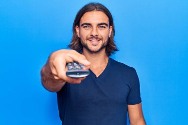 Uzaktan kumandalı yakışıklı genç adam pozitif ve mutlu görünüyor. Duruyor ve gülümsüyor. Kendine güvenen bir gülümsemeyle dişlerini gösteriyor. 