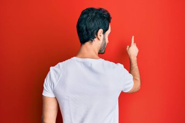 Gündelik beyaz tişört giyen genç İspanyol adam, parmak eliyle öne doğru poz veriyor. 