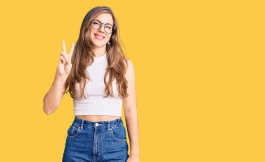 Güzel, beyaz, günlük kıyafetler ve gözlük takan genç bir kadın iki numaralı parmaklarıyla kendini beğenmiş ve mutlu gülümserken onu gösteriyor.. 