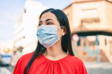 Tıbbi maske takan genç Latin kız şehirde yürüyor..