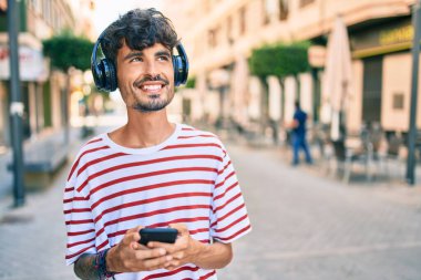 Şehrin caddesinde yürüyen, kulaklık ve akıllı telefon kullanan genç bir İspanyol..