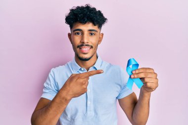 Genç Arap yakışıklı adam mavi kurdele tutuyor gülümsüyor mutlu el ve parmak ile işaret ederek 