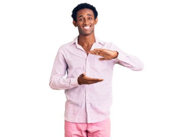 Sıradan pembe gömlekler giyen Afrikalı yakışıklı bir adam. Ellerinde büyük ve büyük boy işareti olan bir jest. Ölçüm sembolü. Kameraya bakıp gülümsüyor. ölçüm kavramı. 