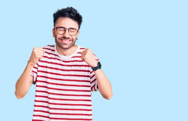 Gündelik kıyafetler giyen genç İspanyol adam başarı için heyecanlı kolları havada ve gözleri kapalı zaferi kutlarken gülümsüyor. Kazanan konsept. 