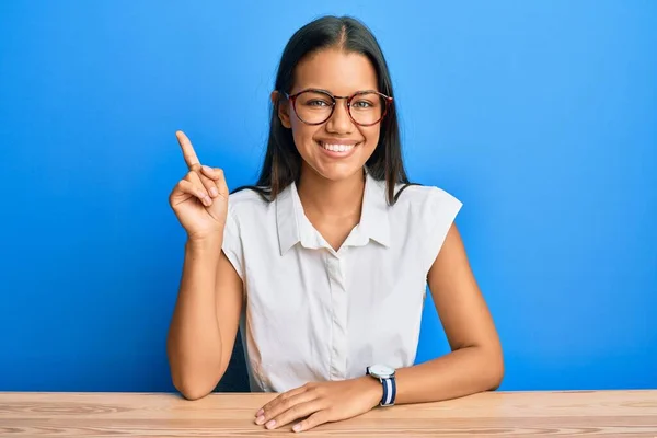 美丽的他的惊慌失措的女人穿着休闲装坐在桌子上 用第一指尖指着桌子 面带微笑 自信而快乐 — 图库照片