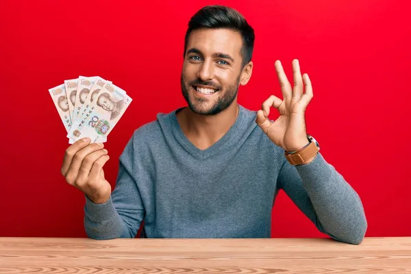 Hombre Hispano Guapo Sosteniendo Billetes Chinos Yuan Haciendo Signo Con —  Fotos de Stock