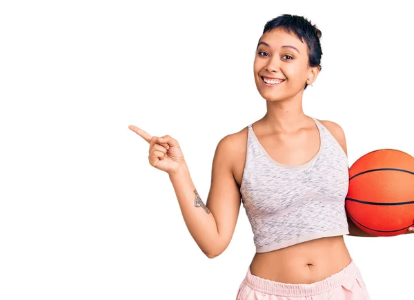 Młoda Kobieta Trzyma Piłkę Koszykówki Uśmiecha Się Szczęśliwy Wskazując Ręką — Zdjęcie stockowe