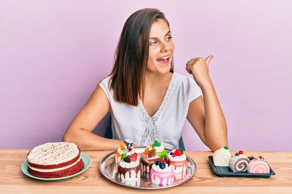 Young Caucasian Woman Eating Pastries Pointing Thumb Side Smiling Happy — Stock Photo, Image