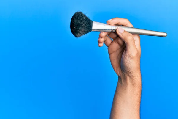 Mano Hombre Hispano Sosteniendo Cepillo Maquillaje Sobre Fondo Azul Aislado — Foto de Stock