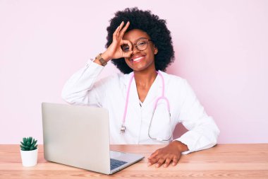 Doktor steteskobu takan Afro-Amerikalı genç bir kadın bilgisayarla çalışıyor gülümsüyor ve mutlu mesut gülümsüyor. 