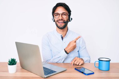 Ofiste çalışan yakışıklı İspanyol bir adam. Operatör kulaklığı takıyor. Gülümsüyor. 