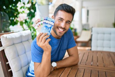 Genç İspanyol gülümseyen adam Kanada dolarlarını terasta tutuyor..