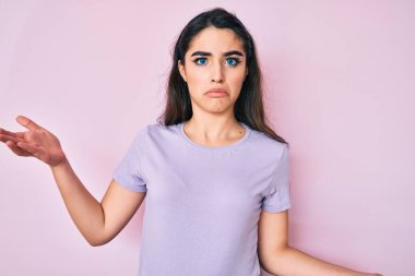 Esmer, sıradan kıyafetler giyen, elleri ve kolları havada, kafası karışmış bir genç kız. şüphe kavramı. 