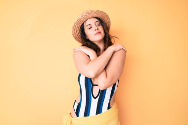 Genç, güzel esmer kadın bikini ve yaz şapkası takıyor mutlu ve pozitif, kendinden emin gülümsüyor. Sevgi ve özgüven. 