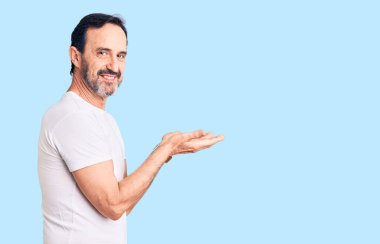 Orta yaşlı, sıradan tişörtler giyen yakışıklı bir adam avuçları açık, fotokopi alanını gösteren, gülümseyerek mutlu bir gülümseme sunan, 