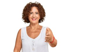 Güzel, orta yaşlı olgun bir kadın, günlük beyaz gömlekler giyip dostça bir şekilde el sıkışarak hoş geldin diyor. başarılı iş. 