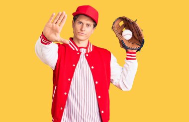 Beyzbol forması giyen yakışıklı genç adam elinde golve topu açık elle tutuyor dur işareti yapıyor ciddi ve kendinden emin bir ifadeyle, savunma hareketi yapıyor. 