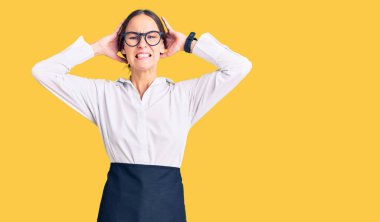 Güzel, esmer, profesyonel garson önlüğü giymiş çılgın ve elleri başında korkmuş ağzı açık bir şekilde şok geçirmekten korkan genç bir kadın. 