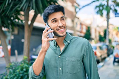 Genç Latin adam gülümsüyor ve şehirde akıllı telefondan konuşuyor..