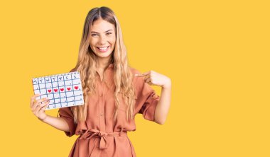 Güzel, beyaz, sarı saçlı, kalp takvimiyle gülümseyen, mutlu ve gururlu bir kadını gösteren bir takvim. 