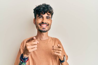 Günlük kıyafetler giyen genç İspanyol adam mutlu ve komik yüzüyle kamerayı işaret ediyor. iyi enerji ve titreşimler. 