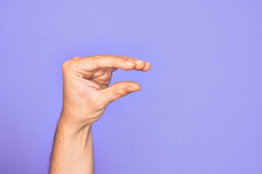 İzole edilmiş mor arka plan üzerinde parmaklarını gösteren beyaz bir adamın eli. Görünmez bir şeyi alıyor, parmakları boşluğu gösteren bir nesneyi tutuyor.
