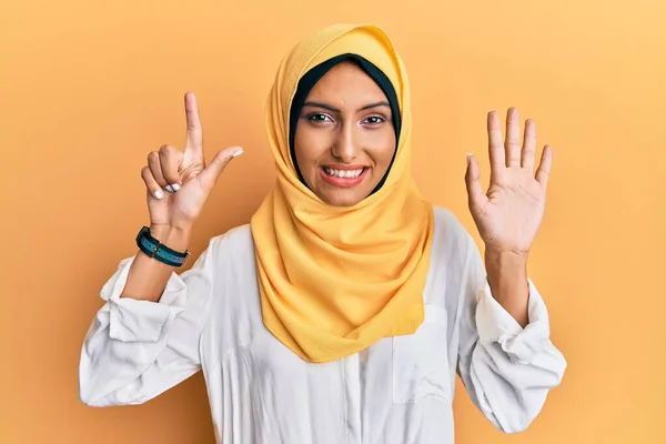 若いですブルネットArab女性身に着けています伝統的なイスラムヒジャーブスカーフ見せますと指番号7で指摘しながら 自信と幸せ — ストック写真