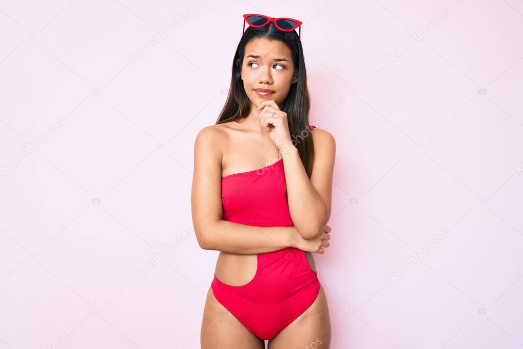 Young beautiful latin girl wearing swimwear thinking concentrated about doubt with finger on chin and looking up wondering 