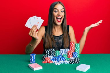 Genç İspanyol kadın masada oturmuş poker oynuyor başarıyı mutlu bir gülümsemeyle kutluyor ve kazanan el kaldırarak ifade ediyor. 