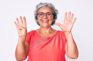 Son sınıf Latin kökenli, gri saçlı, günlük kıyafetler giyen, gözlüklü, dokuz numaralı parmaklarıyla işaret eden mutlu ve kendinden emin bir şekilde gülümseyen kadın.. 