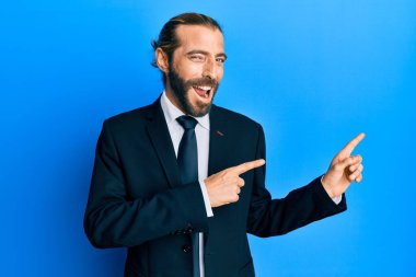 Uzun saçlı, sakallı, takım elbiseli, kravatlı, gülümseyen ve kameraya bakan çekici bir adam.. 