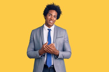 Afro saçlı, elleri bağlı iş ceketi giyen ve rahat ve neşeli gülümseyen yakışıklı Afro-Amerikan erkeği. Başarı ve iyimserlik 