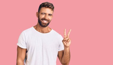 Gündelik beyaz tişört giyen, kameraya gülümseyen ve zafer işareti yapan İspanyol genç adam. İki numara.. 