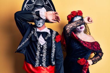 Meksikalı genç bir çift, ölü kostümünü giyip sarıya boyanmış kollarıyla gözlerini kapatıyor, ciddi ve üzgün görünüyorlar. Görme, saklama ve reddetme konsepti 