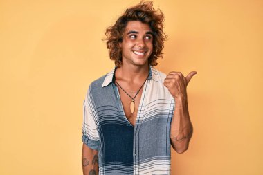 Yaz stili giyinmiş, gülümseyen, mutlu yüzlü genç bir adam başparmağıyla yan tarafa bakıyor ve işaret ediyor.. 
