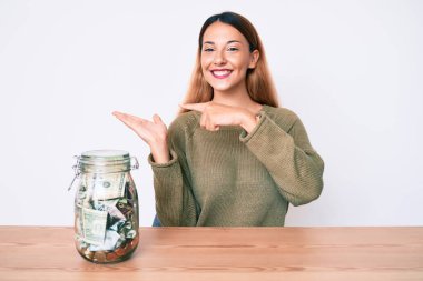 Genç esmer kadın elinde dolarlarla masada oturuyor kameraya hayret ediyor ve gülümsüyor.. 