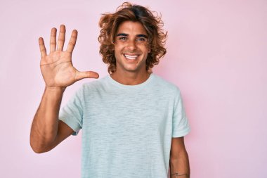 Gündelik kıyafetler giyen genç İspanyol adam beş numarayı gösterip işaret ederken kendinden emin ve mutlu bir şekilde gülümsüyor.. 