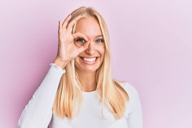 Sıradan kıyafetler giyen genç sarışın kız el hareketleriyle gülümsüyor, mutlu yüzle parmaklarının arasından bakıyor.. 