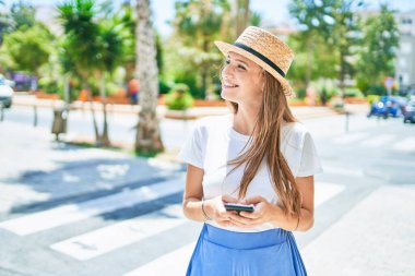 Genç sarışın kadın tatilde gülümsüyor. Şehrin caddesinde akıllı telefon kullanıyor.