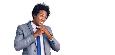 Afro saçlı, iş ceketi giymiş, elleri çenesinde gergin ve heyecanlı bir şekilde gülümseyen yakışıklı Afro-Amerikalı bir adam. 