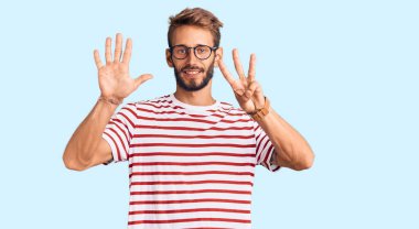 Sakallı, sıradan kıyafetler giyen ve gözlüklü yakışıklı bir adam. Sekiz numaralı parmaklarıyla işaret ediyor. Kendinden emin ve mutlu bir şekilde gülümsüyor.. 