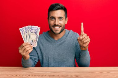 Japon yen banknotları tutan yakışıklı İspanyol bir adam bir fikir veya soru işareti ile gülümsüyor mutlu bir yüzle, bir numara 
