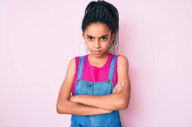 Saçları örgülü, pembe arka planda kuşkucu, gergin ve suratında çapraz kollu tasvip etmeyen bir ifade olan Afro-Amerikan bir kız. negatif kişi. 