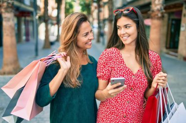 Güzel İspanyol anne ve kızı akıllı telefon kullanıyor ve şehirde alışveriş yapıyor..
