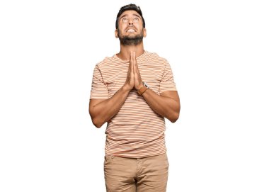 Yakışıklı İspanyol adam gündelik giysiler giyiyor. Elleriyle yalvarıyor ve dua ediyor. Yüzünde umut ifadesi var. Yalvarıyor. 