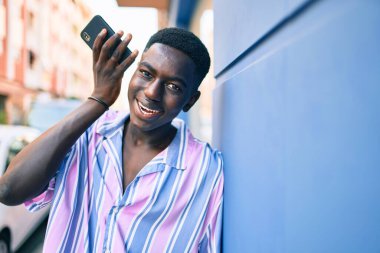 Genç Afrikalı Amerikalı gülümseyen adam şehrin caddesindeki akıllı telefonda mutlu bir şekilde konuşuyor..