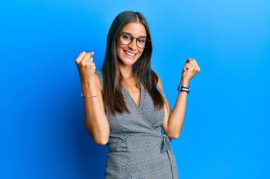 Genç İspanyol kadın iş elbisesi ve gözlük takıyor gururla bağırıyor zaferi kutluyor ve başarıyı kollarını kaldırarak kutluyor. 